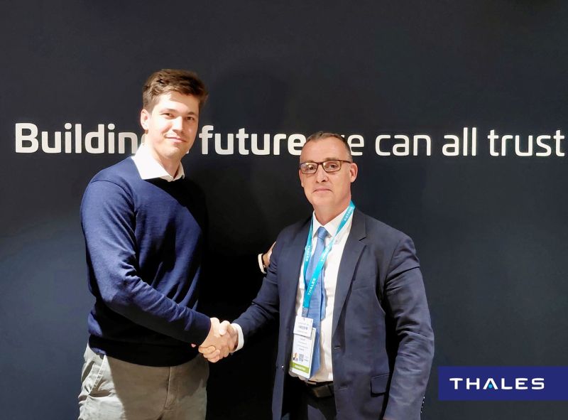 Philipp shaking hands with a Thales executive in front of a 'Building a future we can all trust' backdrop
